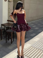 Woman in a burgundy dress standing on a sidewalk with tables and chairs in the background.